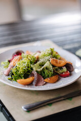 Warm salad with veal and apricots. Delicious food in restaurant. Wooden table