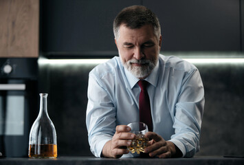 Confident rich mature wealthy businessman chilling relaxing drinking enjoying whiskey in the kitchen after work.