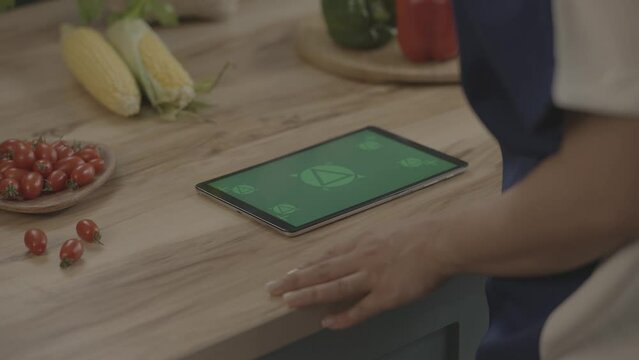 Man in kitchen Holding and watching iPad pro green screen with Fresh food vegetables on countertops. Mock-up for restaurant and food website ,app promo. Camera moving. February2022-Berlin,Germany