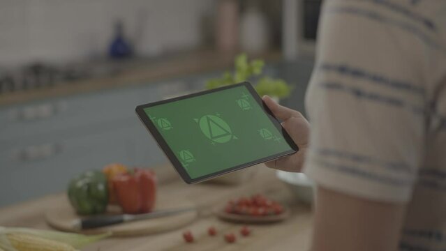 Man in kitchen Holding and watching Android tablet green screen with Fresh food vegetables on countertops. Mock-up for restaurant food website ,app promo. Camera moving. February2022-Berlin,Germany