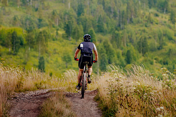 Fototapeta na wymiar back male cyclist rides mountain bike trail on background forest landscape