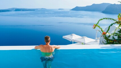 man relaxing in infinity swimming pool during vacation at Santorini, swimming pool looking out over...