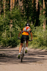 Fototapeta premium back young cyclist with backpack and helmet biking on forest trail
