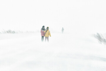 Fototapeta na wymiar Two girls are walking along the road through a snowstorm in the city, the winter is cold..