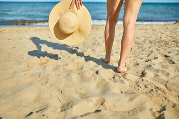 Woman hold in hand straw hat on yhe beach near sea, Summer vacation and travel. Copy space