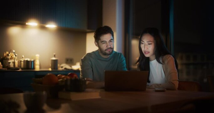 Portrait of Young Couple Using Laptop Computer While Sitting in the Kitchen at Home. Boyfriend and Girlfriend Doing Online Shopping to Renovate the House, Browsing the Internet to Compare Sales