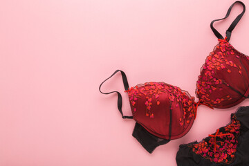 Female dark black red bra and panties on light pink table background. Pastel color. Closeup. Woman underwear set. Romantic lingerie. Empty place for text. Top down view. - obrazy, fototapety, plakaty