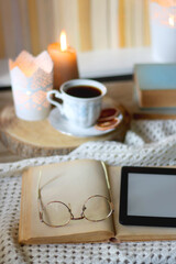 Vintage books, reading glasses, e-reader, cup of tea, bowl of biscuits and lit candle on the table. Selective focus.