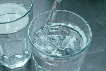 Pouring water from bottle into glass on grey background. Refreshing drink. Healthy lifestyle and stay hydrated