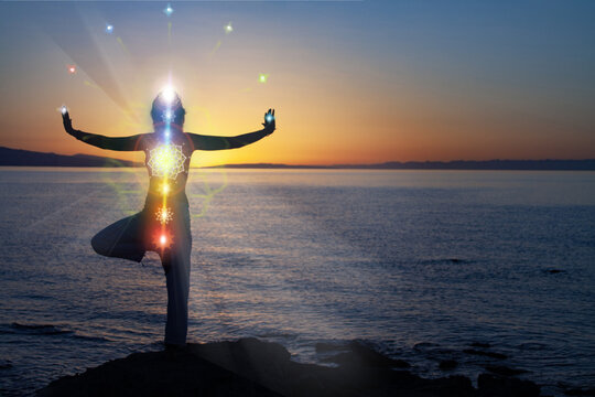 woman in yoga pose on beach sunset view, glowing seven all chakra. Kundalini energy. girl practicing meditation outdoors. Silhouette.