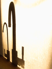 Shadow of kitchen faucet on gray tiles. water tap with long bright shadow. Faucet in warm morning sunlight and shadow