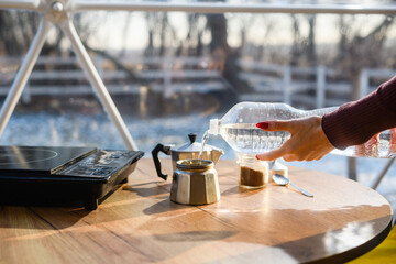 A woman pours water for making coffee in a geyser coffee maker at home.