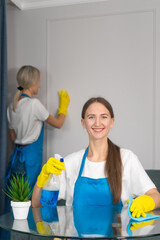 Staff of the cleaning service with professional equipment is engaged in cleaning the house, hygiene. Young woman in uniform wipes the table with a cleaning agent, microfiber cloths. Vertical photo