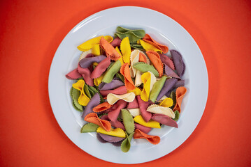 multi-colored raw pasta on a plate on an orange bright background