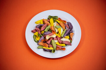 multi-colored raw pasta on a plate on an orange bright background