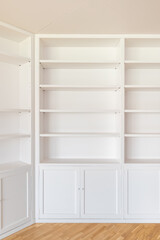 Fototapeta na wymiar White wardrobes from floor to ceiling along the walls in the room. Many shelves for various interior items, books. From below lockers with doors for clothes, bed linen. The floor is wooden parquet.