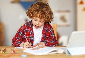 Smiling cute ginger child school boy studying online on tablet at home