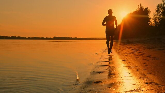 Male silhouette in the rays of the setting sun. Athletic man on the beach. Contrasting image of the beach, river and forest