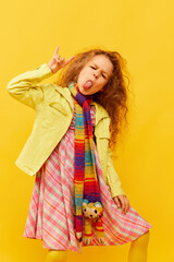 Rock and roll. Little cute girl, child with curly hair emotionally posing in bright clothes over yellow studio background. Concept of childhood, emotions, fun, fashion, lifestyle, facial expression