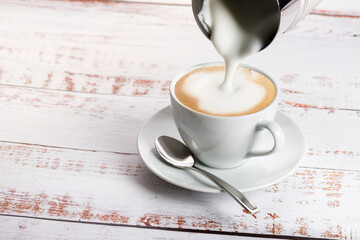 Making cappuccino with milk frother on wooden table. - obrazy, fototapety, plakaty