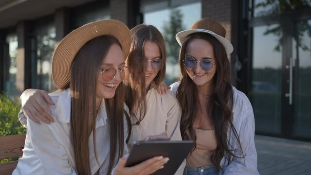Three young beautiful woman girl hipster friends in summer relaxing using digital tablet looking at photo laughing surfing Internet street outdoor. Friendship having fun. happiness freedom love 