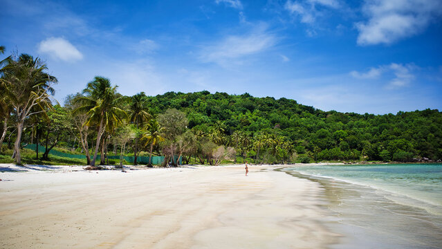 Phu Quoc island, Vietnam - March 31, 2019: White sand beach, calm sea. Rocky hills, growing palms and tropical trees. Beautiful coast of the South China Sea