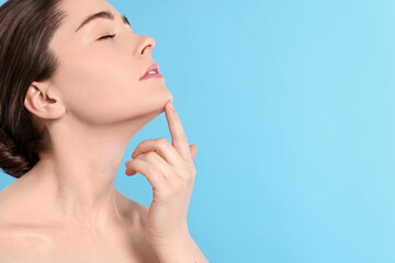 Young woman massaging her face on turquoise background. Space for text