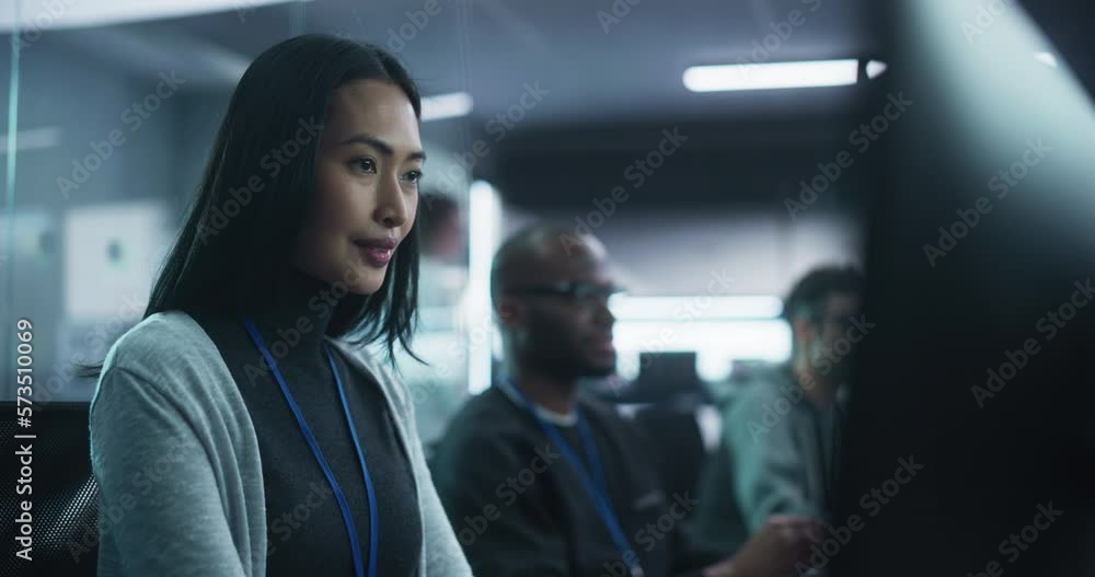 Poster Cinematic Footage of a Beautiful Asian Female Working on a Desktop Computer in a Cyber Security Software Development Department. Positive Brunette Female Lightly Smiling While Working on a Project