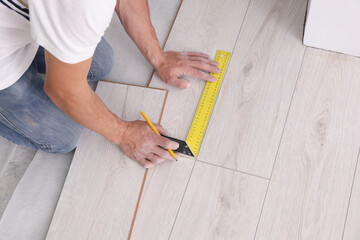 Fototapeta na wymiar Man using measuring tape during installation of laminate flooring, above view