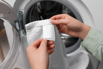 Woman reading clothing label with care symbols and material content on white towel near washing...