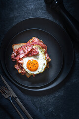 Fried eggs, bacon and toasts on black background. Breakfast concept. Selective focus. Top view. Rustic styje,
