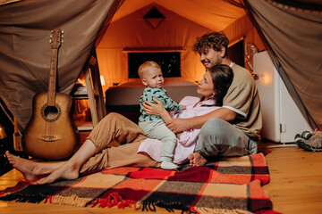 Obraz na płótnie Canvas Happy family with lovely baby playing and spend time together in glamping on summer evening. Luxury camping tent for outdoor recreation and recreation. Lifestyle concept