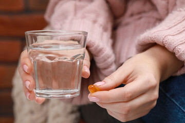 Woman holding glass of water and pill, closeup view