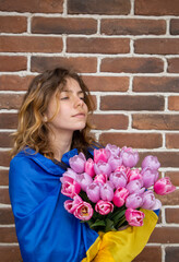 beautiful pensive young woman holding bouquet of pink and lilac tulips. yellow-blue flag of Ukraine is tied behind back. Patriotic gift, bouquet for patriotic girl, gratitude. Mother's Day in Ukraine