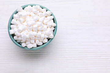 Bowl with delicious marshmallows on white wooden table, top view. Space for text