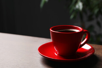 Red cup with aromatic coffee on wooden table indoors. Space for text