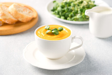 Cup of pumpkin cream soup garnished with fresh sunflower microgreen. Creamy butternut squash autumn soup in elegant white tea cup.  Front view, selective focus