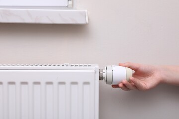 Girl adjusting heating radiator thermostat near white wall indoors, closeup