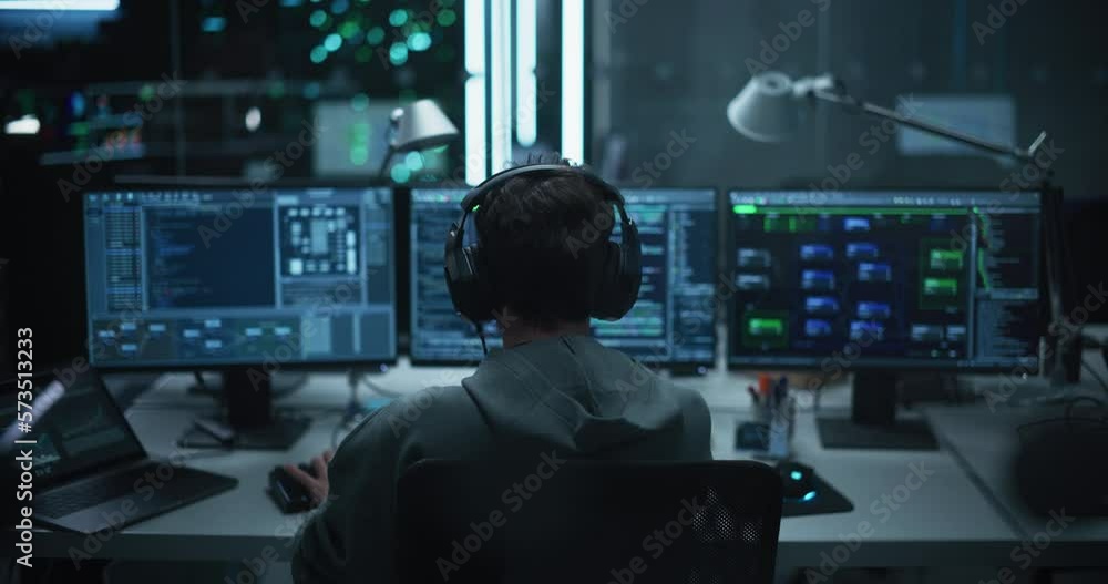 Poster Lone Hacker Breaks Into Government Data Servers and Infects Their System with an Exploit Software. His Hideout Place is in Dark Technological Facility with Multiple Displays. Footage from the Back