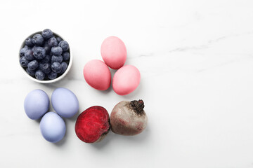 Colorful Easter eggs painted with natural dyes and ingredients on white marble table, flat lay. Space for text