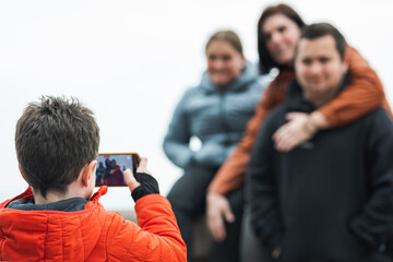 Elementary caucasian kid photographing his family with a mobile phone