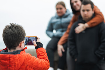 Elementary caucasian kid photographing his family with a mobile phone