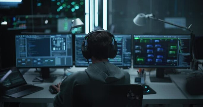 Lone Hacker Breaks Into Government Data Servers and Infects Their System with an Exploit Software. His Hideout Place is in Dark Technological Facility with Multiple Displays. Footage from the Back