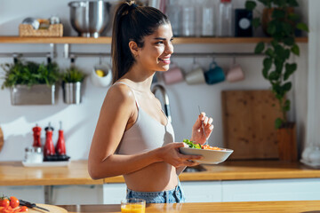 Fintess woman eating a healthy poke bowl in the kitchen at home.
