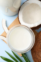 Glass of delicious vegan milk, coconuts and leaf on light blue background, flat lay