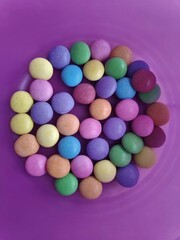 Caramelos de colores dentro de un bol de color púrpura encima de una bandeja de madera