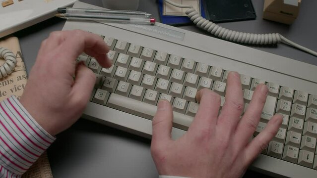 Male hands with pinstripe shirt cuffs typing on a retro 1980s word processor keyboard.