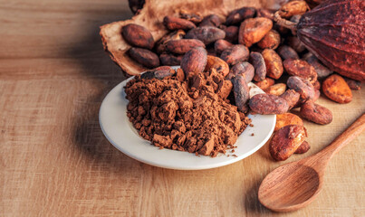 Cocoa powder and cocoa beans with cocoa pods on wooden background.