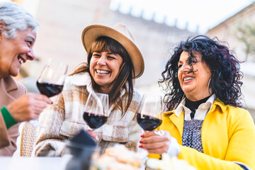 Happy women drinking and toasting red wine outdoors at bar restaurant-Mature senior people having fun together at bistrò pub-Group of female friends hanging out on city-Life style and laughing concept