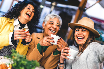 Group of mature women having  fun at the café bar enjoying breakfast drinking coffee- Three senior female  taking selfie with smart phone outdoors at cafeteria dehor-Life style concept 